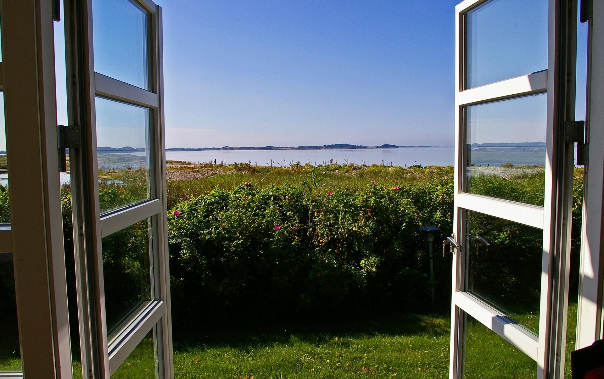 Puertas practicables de aluminio abiertas donde se puede apreciar el bonito paisaje verde y la playa