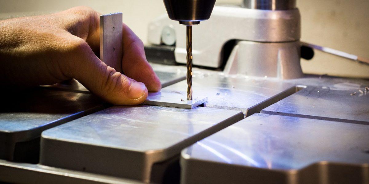 Trabajador con taladro haciendo agujeros en una base de metal pequeña